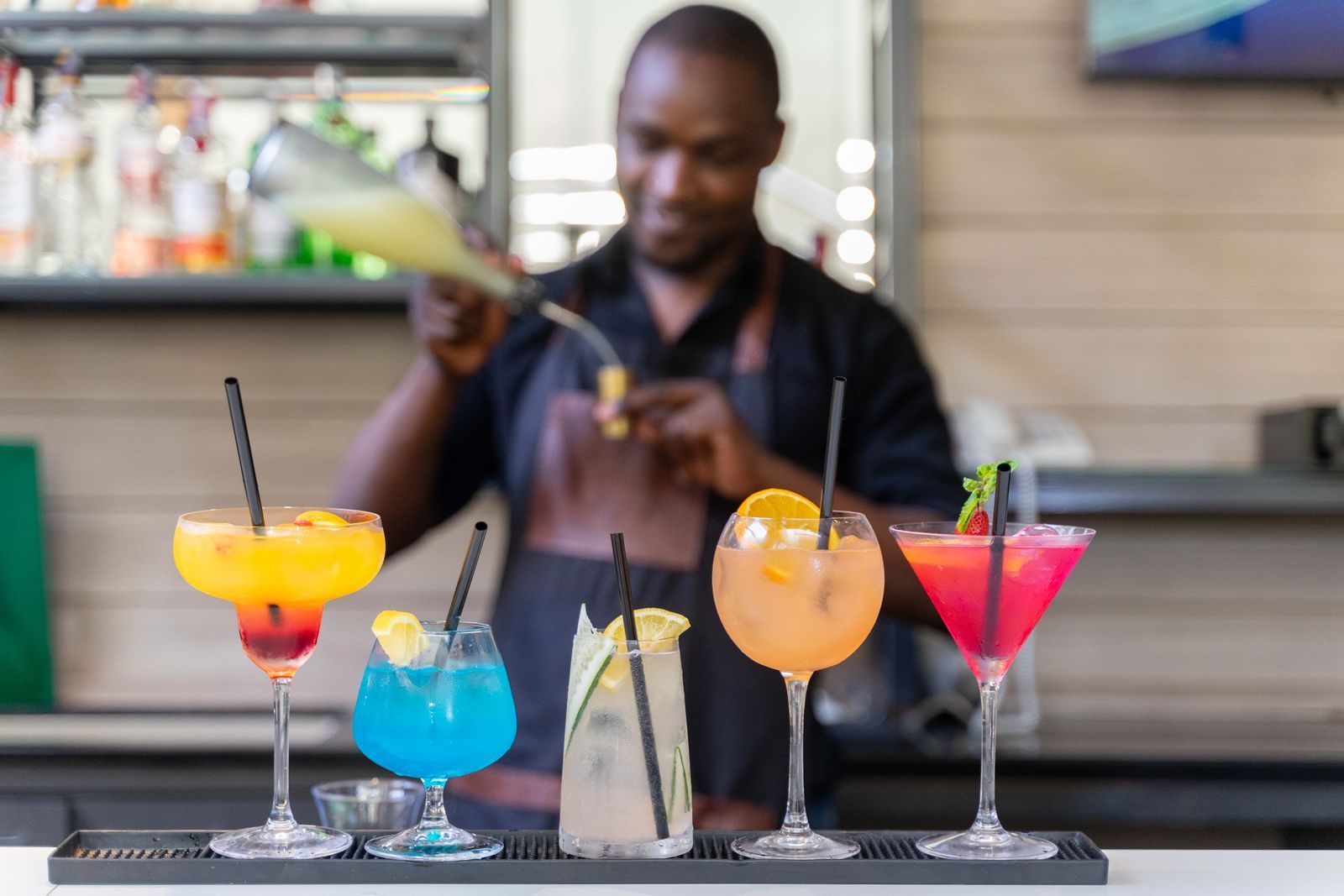 A bartender finishing a row of colorful cocktails, the drinks many all inclusive cruises bundle