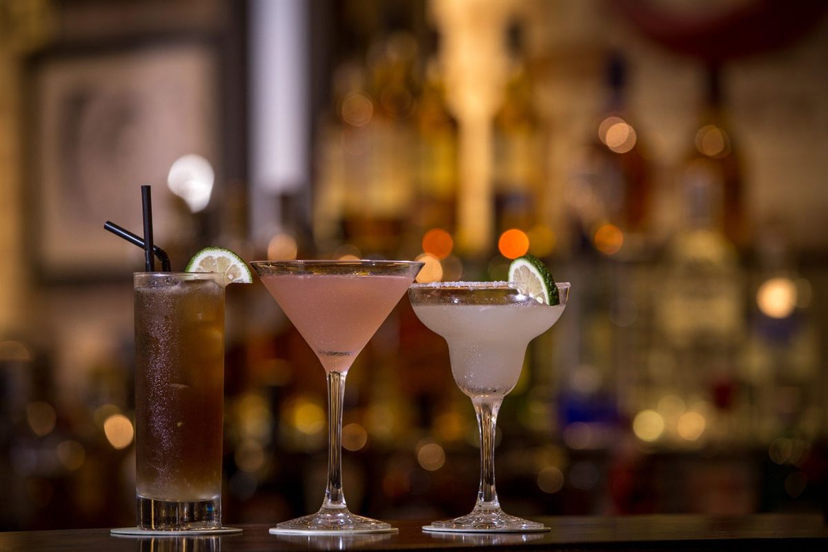 Three cocktails with citrus garnish on a bar counter in warm evening light
