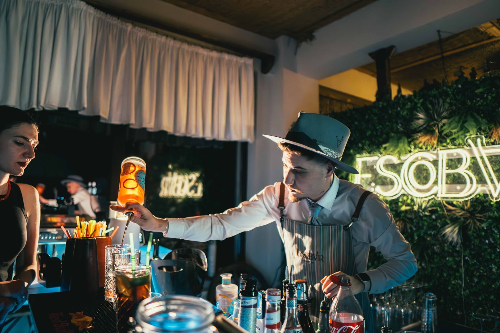 A bartender in a hat pouring drinks at a lively bar, the classic a la carte cruise extra