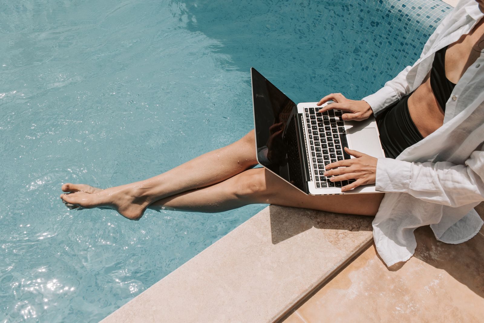 A traveler typing on a laptop at the edge of a pool, working out how much a cruise really costs