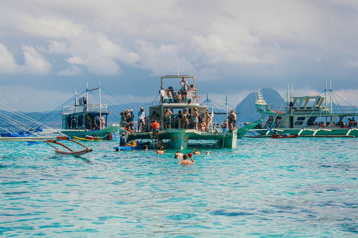 Tour boats and swimmers in clear turquoise water near a tropical island