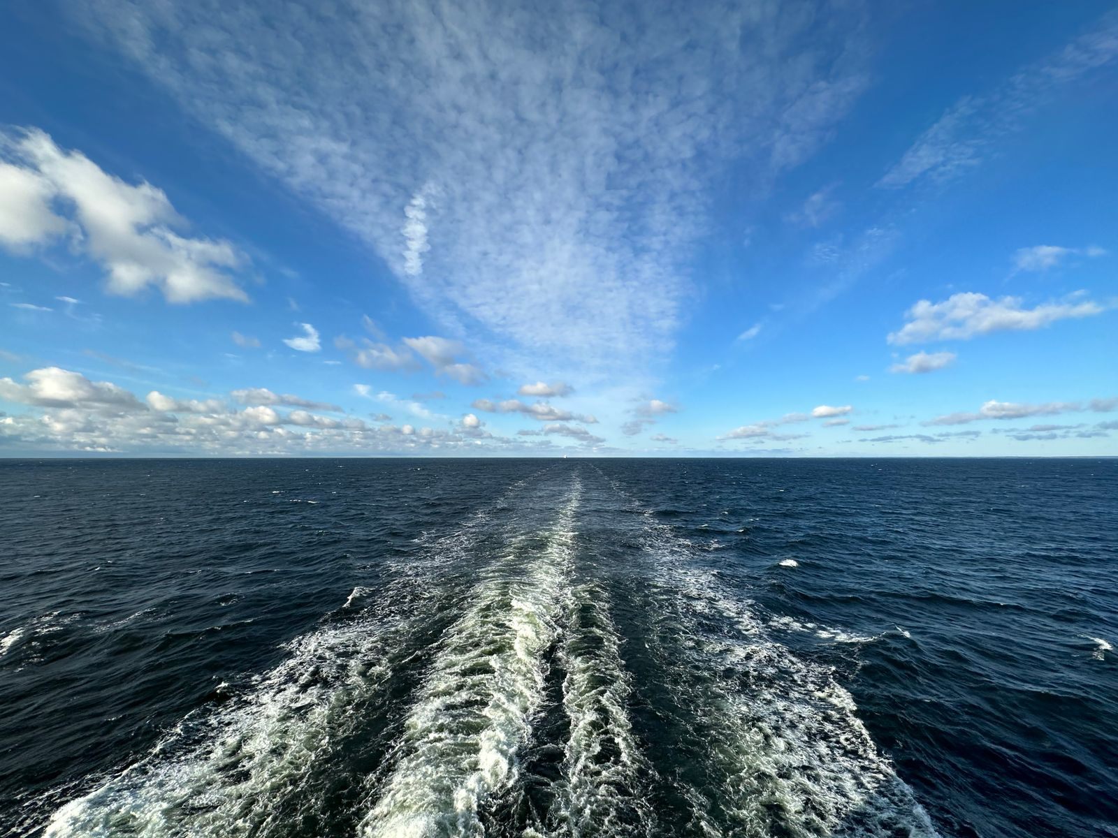 The white wake of a cruise ship stretching across a deep blue sea, the voyage all inclusive cruises and a la carte fares both pay for