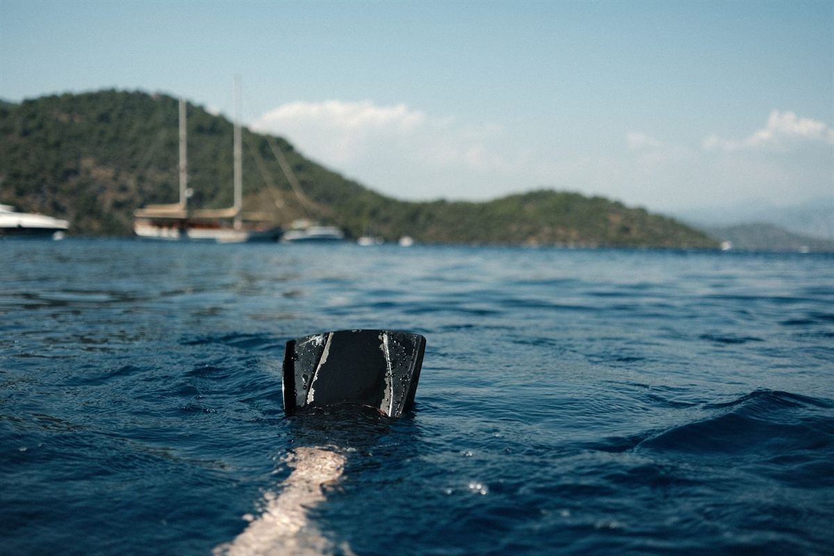 A snorkeler floating in a calm bay with sailing boats and green hills behind